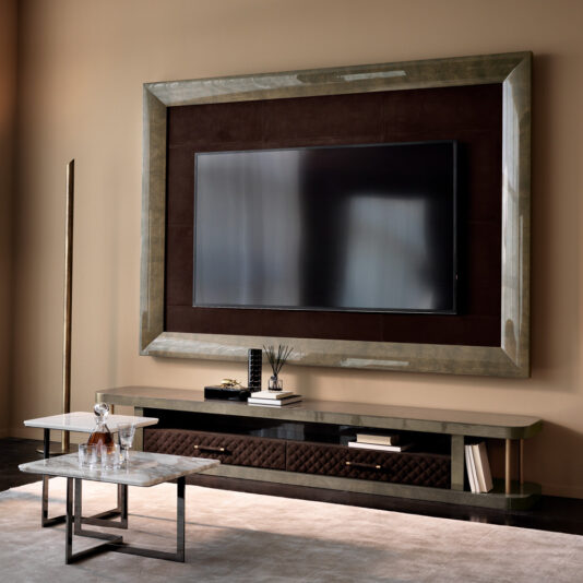 A modern living room highlights the Italian Designer Media Unit With TV Wall Frame displaying a large flat-screen TV, complemented by a console table with decor and glassware, and two marble-topped coffee tables in front.
