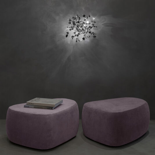 Contemporary Italian Designer Wall Light Two purple ottomans sit before a dark gray wall, one holding books. Above them, the Contemporary Italian Designer Wall Light casts abstract shadows and softly illuminates the wall.