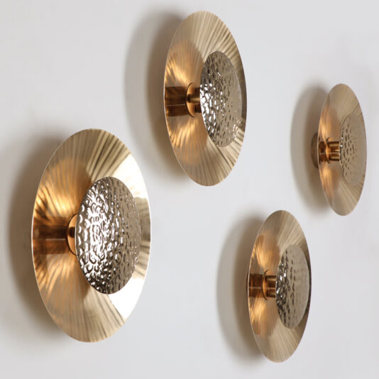 Four Designer Gold Plated Hammered Round Wall Lights adorn a light grey wall. Each features a circular, gold-plated, textured disc with a hammered pattern at the center, creating a visually striking and elegant design. The discs vary slightly in their angles and positions.