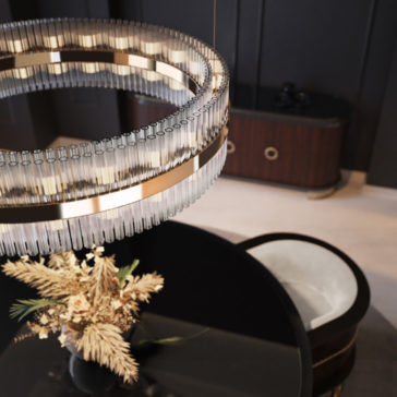 Contemporary Designer Tiered Chandelier A modern dining area featuring the Contemporary Designer Tiered Chandelier, characterized by cascading glass elements, hanging above a black glossy dining table. Below this impressive chandelier sits a vase with dried flowers. In the background is a dark wooden sideboard adorned with gold accents.