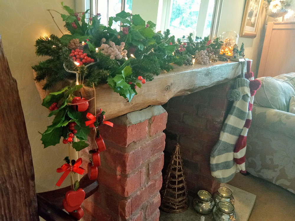 Christmas mantelpiece with foliage, berries, lights and wooden hanging apples