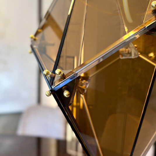 Modern Champagne Prism Glass Pendant A close-up of the Modern Champagne Prism Glass Pendant shows its contemporary, angular design with amber-tinted panels, black metal edges, and gold bolts. The softly blurred background emphasises the pendant's modern elegance.