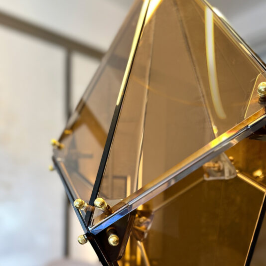 Modern Champagne Prism Glass Pendant A close-up of the Modern Champagne Prism Glass Pendant showcases its geometric amber glass and metallic gold accents, set against a softly blurred indoor background.