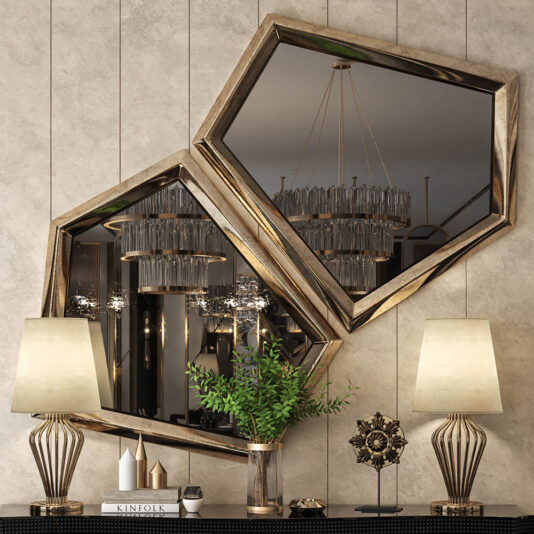 The Exclusive Pair Of Art Deco Inspired Mirrors with gold frames hang above a console table displaying modern lamps, a potted plant, sculpture, and a book; chandeliers reflect in the mirrors on a textured wall.