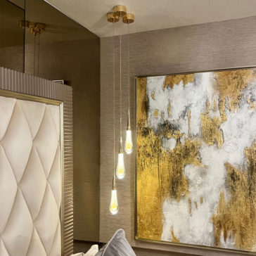 Set of 3 Glass Drop Pendant Lights A modern bedroom showcases a tufted headboard accompanied by the Set of 3 Glass Drop Pendant Lights, which feature teardrop-shaped bulbs and hang from the ceiling at different lengths beside a large abstract painting adorned with white and gold textures.