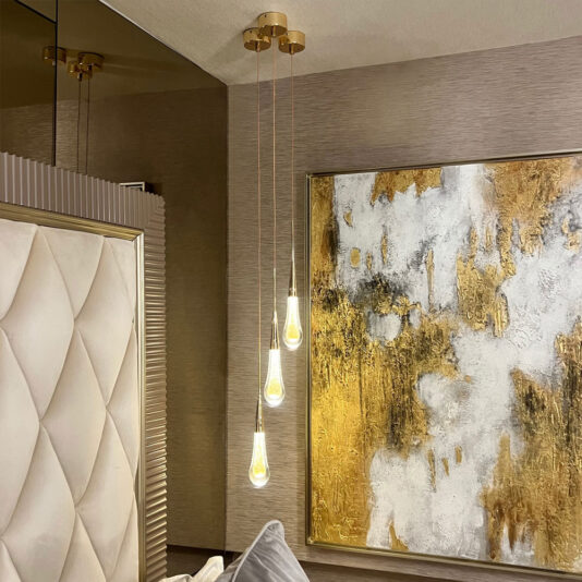 A modern bedroom showcases a tufted headboard accompanied by the Set of 3 Glass Drop Pendant Lights, which feature teardrop-shaped bulbs and hang from the ceiling at different lengths beside a large abstract painting adorned with white and gold textures.