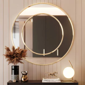 A Contemporary Round Wall Mirror with a smaller concentric circle mirror hangs on a beige-paneled wall. Below, a black cabinet showcases a black and white vase with dried plants, a small sculpture of a horse, and a minimalistic lamp with a spherical light.