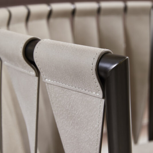 Close-up of the backrest of the Luxury Modern Leather Twist Armchair, featuring exquisite beige suede-like upholstery and a sleek dark wooden frame. The backrest showcases a distinctive folded-over design with visible stitching details, highlighting its contemporary and elegant craftsmanship.