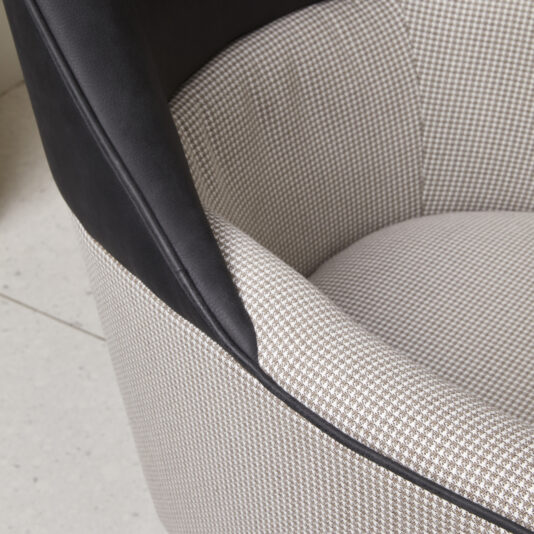 Modern High Backed Occasional Armchair Close-up of the Modern High Backed Occasional Armchair featuring a black leather backrest and an upholstered seat and interior with a small checkered pattern in shades of beige and white. The armchair is positioned on a light-colored tiled floor.