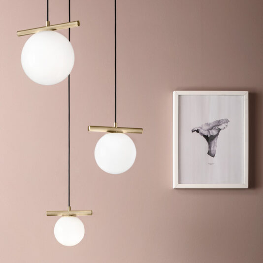 A minimalist interior is adorned by the Modern Murano Glass Pendant Light Cluster, which features glowing glass pendants with brass fixtures hanging at varying lengths against a muted pink wall. To the right, a framed sketch of a bird perched on a branch completes the look.