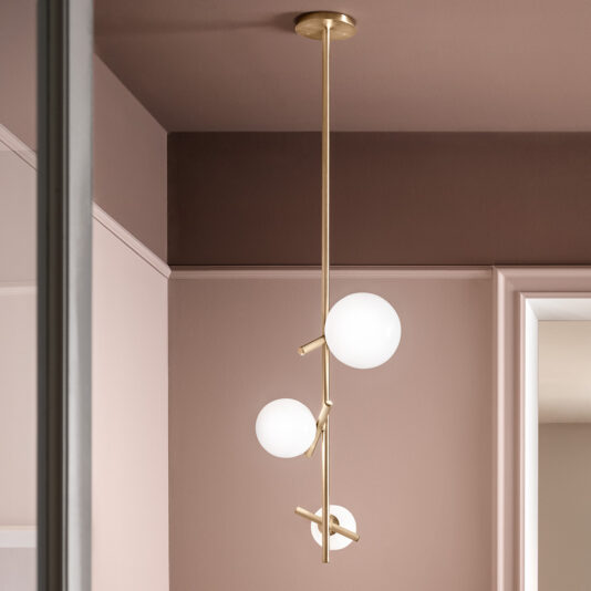 A stunning *Contemporary Murano Glass Vertical Pendant Light* hangs gracefully from the ceiling, featuring a brass fixture with three arms, each topped with a round, white lampshade. The elegant setting is further enhanced by light pink walls and a glimpse of either a white-framed mirror or doorway in the background.