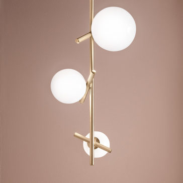 Introducing the Contemporary Murano Glass Vertical Pendant Light, a stylish fixture with a gold rod adorned by three white, spherical glass lamps arranged at different angles. Set against a muted mauve-colored wall, this light accentuates modern elegance.