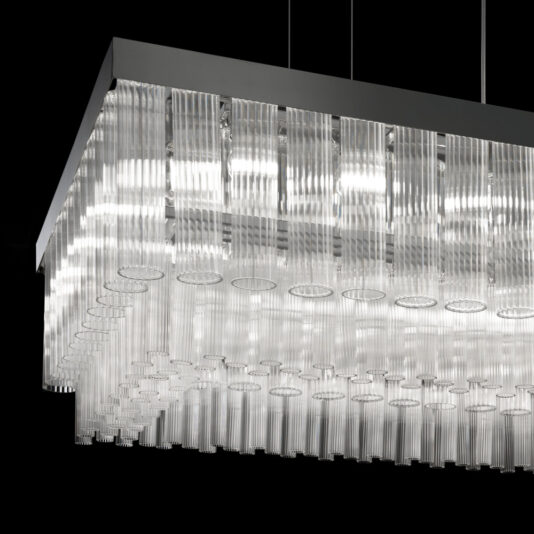 Contemporary Venetian Glass Rectangular Chandelier Introducing the Contemporary Venetian Glass Rectangular Chandelier: This stunning lighting piece features a sleek, dark frame from which multiple clear, cylindrical Venetian glass rods hang vertically. The rods vary in length, creating an elegant tiered effect. When illuminated, the chandelier casts a bright, diffused light that enhances any modern space.