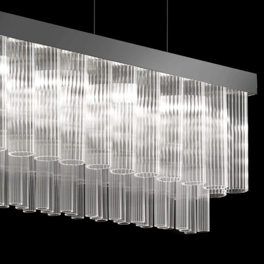 The Contemporary Glass Chandelier, with its sleek modern design, features multiple hanging glass tubes of varying lengths that emit a white, ambient glow against a black background, enhancing the minimalist aesthetic.
