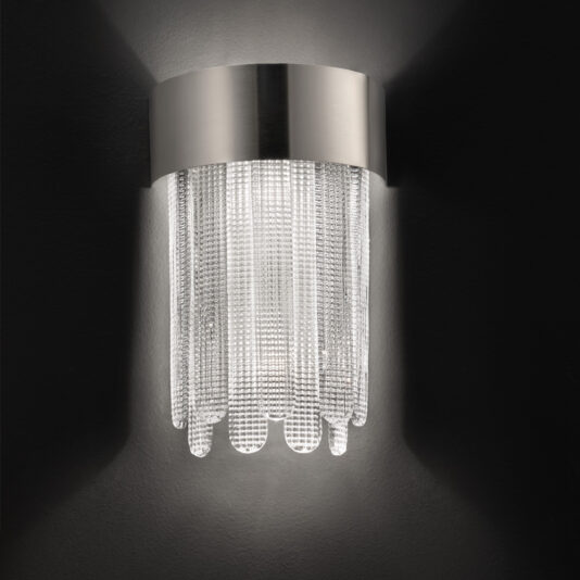 The Contemporary Venetian Glass Wall Light features a modern wall sconce design, characterized by a sleek, cylindrical stainless steel top complemented by cascading crystal strands. It emits a soft, warm glow against a dark background.