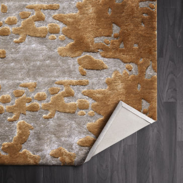 High Quality Abstract Hand Woven Rug A close-up shot showcases a corner of the High Quality Abstract Hand Woven Rug, highlighting its light grey base adorned with copper brown abstract patterns. The folded-over corner reveals a plain, light grey underside, and the rug is laid on a dark wooden floor.