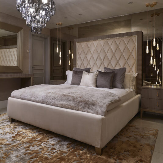 Luxurious bedroom with a large upholstered bed, diamond-tufted headboard, and several pillows. A modern chandelier hangs from the ceiling, ambient lighting is provided by hanging pendant lights, and a High Quality Abstract Hand Woven Rug adds warmth. A large mirror and vanity table are on one side.