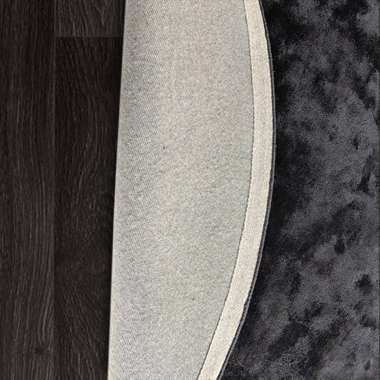 A partially rolled-up High Quality Hand-Woven Round Rug on a dark wooden floor showcases the rug's gray underside and its plush, dark textured surface.