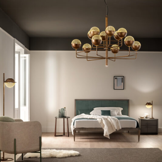 Large Modern Round Pendant Chandelier A modern bedroom equipped with a Large Modern Round Pendant Chandelier featuring multiple lights. The room showcases a bed with a green upholstered headboard, two nightstands, a beige armchair, and minimalistic decor. Natural light pours in from a tall window, illuminating the space.