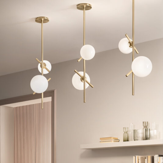 Modern Murano Glass Vertical Pendant Light A modern interior showcases a Modern Murano Glass Vertical Pendant Light with spherical white bulbs suspended from the ceiling. Below, a shelf filled with books and decorative glassware is mounted on a beige wall. The room embodies a minimalist aesthetic with a neutral color palette.