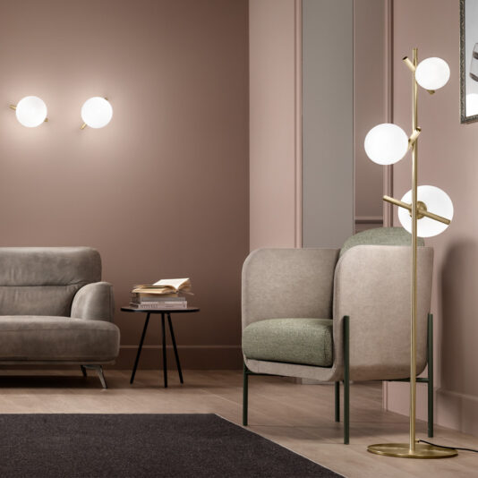 Modern Murano Glass Floor Lamp A modern living room with muted pink walls featuring two wall-mounted round lights, a gray sofa, an armchair with green and beige upholstery, and a stylish Modern Murano Glass Floor Lamp showcasing three globe lights. A small round side table with stacked books adds a cozy touch.