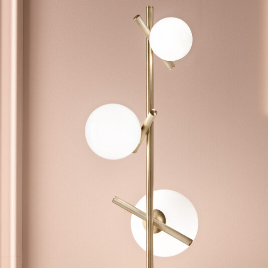 Modern Murano Glass Floor Lamp The Modern Murano Glass Floor Lamp boasts a gold metallic stand with three white spherical bulbs arranged at varying heights. Its sleek and contemporary design is elegantly showcased against a light pink wall.