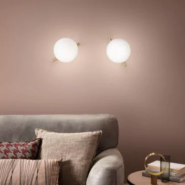 Modern Murano Glass Wall Light A modern living room showcases a gray sofa adorned with textured and patterned throw pillows. Mounted on the wall behind the sofa, two Modern Murano Glass Wall Lights emit a soft glow and are evenly spaced. Beside the sofa, on the side table, rests a small pile of books and a decorative object.