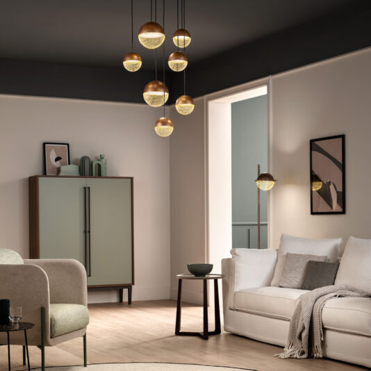 Modern Pendant Drop Cluster Chandelier A contemporary living room showcases a white sofa adorned with a combination of light and dark pillows, accompanied by a cozy blanket. A small round side table is positioned close by. Hanging from the ceiling is the eye-catching Modern Pendant Drop Cluster Chandelier, providing striking modern lighting. Additionally, the space features a minimalist cabinet and various wall art pieces.