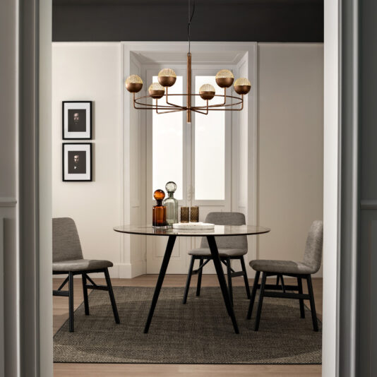 Modern Round Pendant Chandelier A modern dining room boasts a round table set for four, complemented by gray upholstered chairs. Hanging above the table is the Modern Round Pendant Chandelier, featuring textured lights that add a contemporary touch. The room's white walls are adorned with two framed photos, and a large window with sheer curtains allows natural light to fill the space. A gray rug beautifully covers the wooden floor.