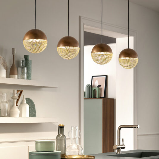 A contemporary kitchen showcasing three stunning Modern Round Pendant Lights with elaborate golden mesh designs. The sink is prominently displayed in the foreground, while white shelves adorned with decorative jars and vases are mounted on the wall. A doorway in the background provides access to another room.