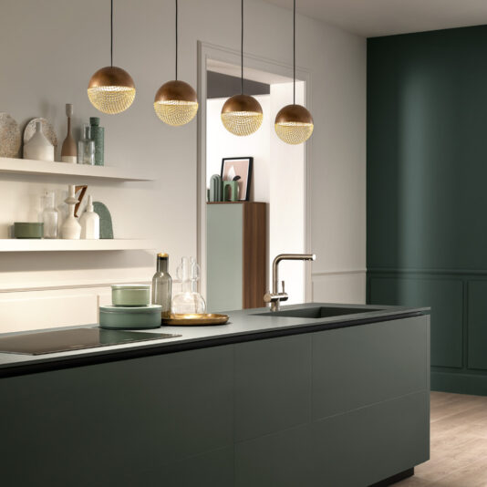 Modern Round Pendant Light Modern kitchen with green cabinetry, black countertops, and gold spherical pendant lights. Minimalistic decor includes shelves with pastel-colored jars and vases. The sink island features a gold faucet and glassware. Walls in white and dark green shades complement the Modern Round Pendant Light design.