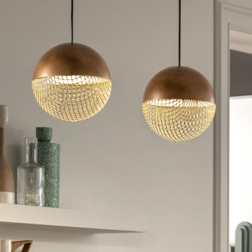 Two Modern Round Pendant Lights with a metallic mesh design hang from the ceiling, casting warm light. In the background, a white shelf holds decorative items including a green textured vase, a beige vase, and a clear glass bottle.