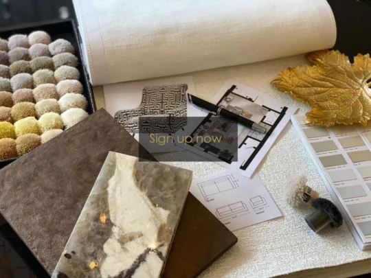 A workspace with interior design materials, including a sample book of fabric swatches, a roll of wallpaper, architectural plans, tile samples, and a golden leaf decor piece. Perfect for planning your dream space with al-fresco entertaining tips—”Sign up now” to get started!