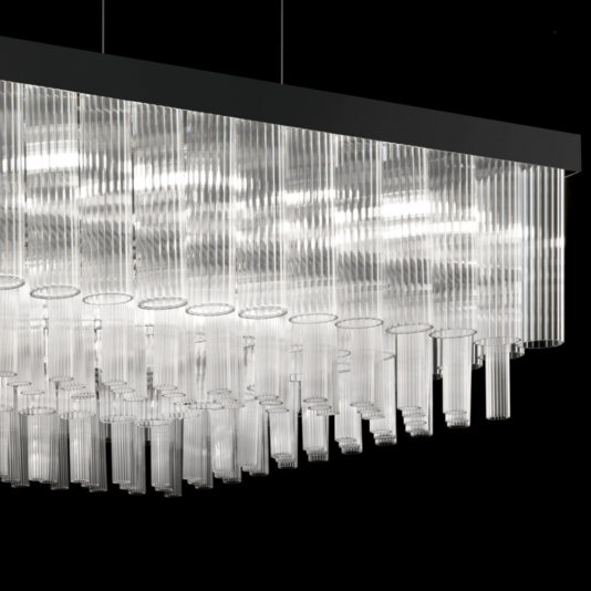 Contemporary Venetian Glass Rectangular Chandelier The Contemporary Venetian Glass Rectangular Chandelier features numerous vertical Venetian glass rods hanging from a sleek black frame. The varying lengths of the glass rods create a stunning tiered effect, while the chandelier emits a bright, even light against a dark background.