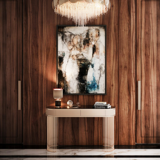 A warmly lit hallway showcases the Modern Art Deco Style Console Table, characterized by its vertical slats and topped with books, a lamp, and a decorative item. Above the table hangs an abstract painting in earthy tones. The space is framed by wooden paneling and illuminated by a crystal chandelier.