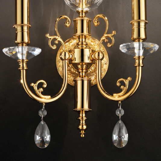 A close-up image showcases the Classic Transparent Gold Wall Light, featuring two candle-like arms adorned with intricate detailing. Several transparent crystal accents embellish the design, including teardrop-shaped pendants gracefully hanging from each arm. The dark background enhances the elegance of this wall light.