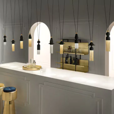 Contemporary Black LED Pendant Light Cluster A modern bar features a sleek, white counter with a golden tray holding glasses and a decanter. Multiple Contemporary Black LED Pendant Light Clusters with tassel-like designs hang from the ceiling. A golden shelf in the background holds various bottles, adding a luxurious touch to the minimalist setting.