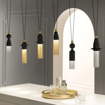 Contemporary Black LED Pendant Light Cluster A modern interior showcases a Contemporary Black LED Pendant Light Cluster arrangement, elegantly suspended in a row above the white countertop. Each pendant light boasts a distinct design, combining black, gold, and glass elements. On the countertop sits an exquisite gold tray with glassware, while a white arched doorway serves as the backdrop.