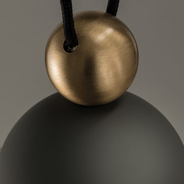 Contemporary Black LED Pendant Light Cluster Close-up of the Contemporary Black LED Pendant Light Cluster showcasing its brushed bronze circular element suspended by two black cords on a smooth, matte black surface. The plain grey background accentuates the contrasting textures and materials of the fixture.