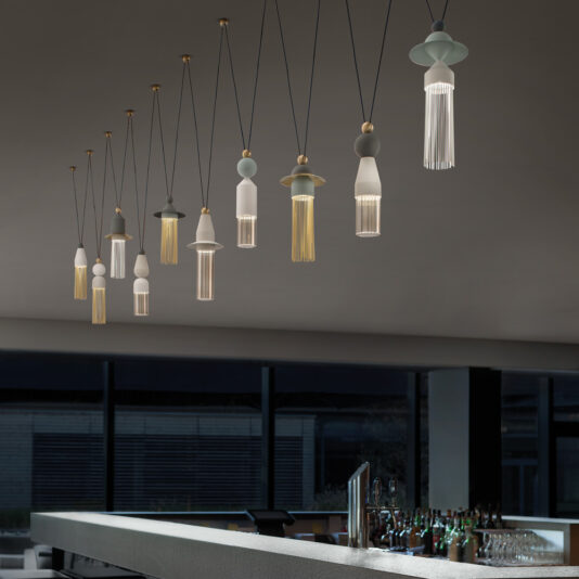 Contemporary Coloured LED Pendant Light Cluster A modern bar interior with a sleek, minimalist design features the Contemporary Coloured LED Pendant Light Cluster. The bar counter is in the foreground, leading to a row of these unique lights hanging from the ceiling. The overall ambiance is stylish and sophisticated.