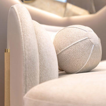 A close-up of the luxurious Contemporary Curved Velvet Sofa, adorned with a textured round throw pillow. The soft and plush fabric enhances its elegant appearance, while a metallic gold accent on the armrest adds a touch of sophistication.