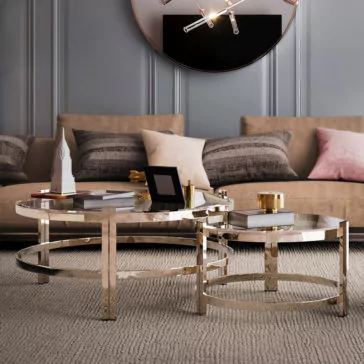 Contemporary Luxury Glass Coffee Tables A contemporary luxury living room features a beige sofa accented with grey and pink pillows. In front of the sofa are two Contemporary Luxury Glass Coffee Tables with gold-colored frames, adorned with decorative items including a small model building, books, and trays.