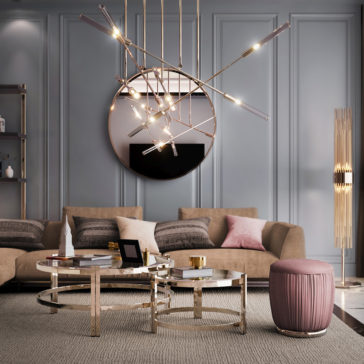 Contemporary Luxury Glass Coffee Tables Modern living room with a beige sectional couch adorned with cushions in grey and pink hues. There's a geometric chandelier, a round wall mirror, Contemporary Luxury Glass Coffee Tables with metallic frames, and a pink upholstered stool on a grey rug, all against a blue-grey wall exuding contemporary luxury.