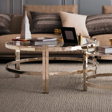 Contemporary Luxury Glass Coffee Tables A sophisticated living room features a beige sofa adorned with patterned pillows. In front stands a sleek, contemporary coffee table from the Contemporary Luxury Glass Coffee Tables collection, featuring elegant gold frame details. The table displays decorative items such as a picture frame, books, and a miniature building model on top of a textured rug.