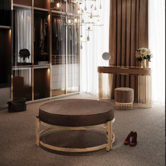 A luxurious dressing room features a large walk-in closet with glass doors, a spacious Contemporary Round Bench with a gold frame, a stylish vanity table with matching stool, modern lighting fixtures, contemporary glass coffee tables, a bouquet of flowers, and a pair of red high-heeled shoes on the carpeted floor.