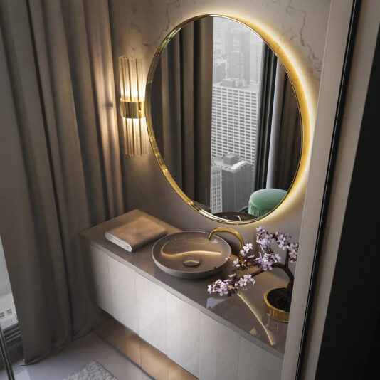 A contemporary bathroom features a large, Contemporary Round Mirror illuminated and mounted on a marbled wall. Below the mirror is a sleek countertop with a towel, a vessel sink, and a small vase of pink flowers. A wall sconce light is to the left, and a cityscape is visible through the window.