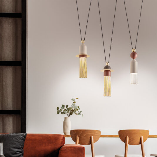 Contemporary Triple LED Pendant Light Three Contemporary Triple LED Pendant Lights hang over a wooden table with two chairs. A minimalist vase with green branches sits on the table. In the foreground, part of a brown sofa is visible. The room has a sleek design with a neutral color palette.