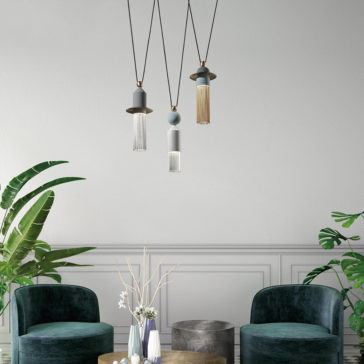 Contemporary Triple LED Pendant Light A modern living room featuring two dark green velvet chairs, a round wooden coffee table, and the Contemporary Triple LED Pendant Light adorned with fringe decorations. The space is enhanced with leafy plants and decorative vases containing dried flowers, set against a light gray wall.