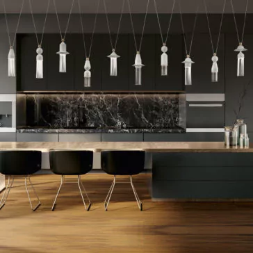 A modern kitchen with a marble backsplash and black cabinets. Overhead, the Contemporary White LED Pendant Light Cluster hangs elegantly. The kitchen island features a wooden countertop with three black chairs, while a vase with branches is placed on the right side of the island.
