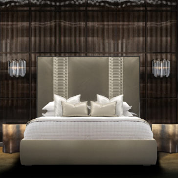 A luxurious bedroom showcases the spacious and elegant Designer Velvet And Satin Interlaced Bed, highlighted by an upholstered headboard adorned with vertical decorative lines. The bed is neatly made with white linens and several pillows, while stylish wall-mounted lamps and an intricate wooden accent wall enhance the sophisticated ambiance.
